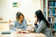© Wanwajee - School students studying together at library table reading textbooks receiving guidance supportive learning environment homework preparation concept.