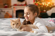 © New Africa - Little girl with her cute cat on bed in room decorated for Christmas