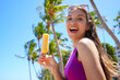 © zigres - Attractive laughing young woman eating popsicle ice pop on the beach with palm trees on the background. Summer holidays concept.