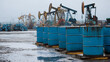 © photo for everything - Oil industry scene with blue barrels lined up in the foreground and oil rigs in the background under a cloudy sky. A landscape of energy and resources.