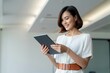 © Macrostock - Mature CEO businesswoman holding digital tablet using fintech tab application standing in office. Eastern Asian 40s adult professional business woman looking digital touchscreen device. Copy space