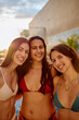© we.bond.creations - Three young women friends smiling at the camera, wearing bikinis, enjoying a summer vacation by the pool at golden hour