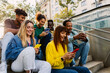 © Xavier Lorenzo - Multiracial group of millennial student friends sitting together outdoors, watching social media content on a smart phone and laughing joyfully. Youth and technology lifestyle concept.