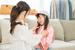 © buritora - A mother helps her daughter get dressed in the living room at home