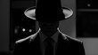 © startang141 - A mysterious man in a fedora hat and suit, with his face obscured by shadow, creating an anonymous and dramatic black and white portrait.