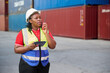 © offsuperphoto - Female worker using a tablet and talking on walkie talkie at container yard