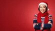 © WAHYU - Smiling Asian woman in Santa hat, red scarf, and Christmas sweater with crossed arms on a red background.