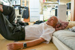 © Masakazu Tokashiki - An older man is laying on a bed with a pillow. He is wearing a white shirt and gray pants