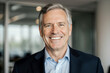 © ThomasLENNE - Close up portrait of mature adult business man with gray hair and suit smiling and looking at camera with succesful attitude. Happy corporate lawyer with white perfect teeth standing at workspace