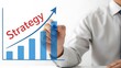 © Pixel Stone - Business professional drawing a bar graph with an upward trend arrow and the word strategy written in red symbolizing growth and planning in a corporate setting with a white background.
