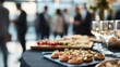 © sablengjago - Guests at a blurred event enjoy an array of hors d'oeuvres on a black tablecloth with drinks in focus