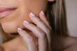 © Марина Демешко - Close-up of young woman touching her cheek with manicured fingers. Natural skin texture, soft light and minimal beauty aesthetic. Skincare, self care and gentle touch concept