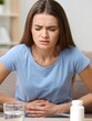 © Pixe lWaves - Woman Holding Stomach in Pain, Medicine and Water on Table