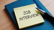© Mudassir - Reminder note clearly displays the words job interview written in dark ink resting on a blue notebook beside a professional pen
