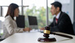 © hardvicore - Judge gavel on courtroom desk, blurred man and woman engaged in mediation, legal discussion.