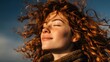 © horizon - Profile of a woman with curly hair enjoying fresh air with closed eyes and wind blowing her hair against a sunny outdoor nature scene.
