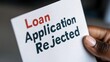 © Virtual Art Studio - A hand holds a white document reading 'Loan Application Rejected,' with 'Loan' in red and the rest in black.