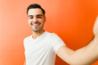 © AntonioDiaz - Smiling young man taking a selfie, showing confident lifestyle and genuine happiness on an orange background