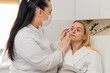 © Andrii Iemelianenko - Middle-aged woman sits in chair while cosmetologist in gloves gently checks facial skin before treatment. Calm adult client in white robe enjoys skincare consultation inside modern beauty clinic room.