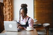 © Serhii - Portrait of an african american young woman sitting at cafe with laptop writing her blog
