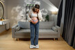 © GRAFStock - Pregnant woman stands on scale measuring her belly with tape measure in living room