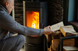© Home-stock - Man stacking firewood near wood stove that burning brightly in room, heating house in cold season