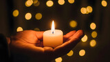 Hand holding lit candle in darkness with bokeh lights