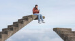 © Rendara Studio - Focused teenager on smartphone sitting on broken stairs in the sky