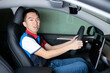 © fotolite - An Asian teenager sits in the driver's seat looking back while reversing, ideal for teen driving safety, parking practice, or driver education concepts.