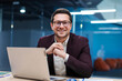 © Home-stock - Charismatic European businessman sitting at desk in stylish office working on laptop and ready for business, smiling at camera