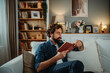 © Dusan - Man relaxing reading book on sofa at home