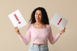 © Pixel-Shot - Happy young African-American woman holding paper sheets with exclamation marks on beige background