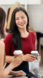 © NAMPIX - Two cheerful Asian businesswomen enjoying a coffee break and chatting in a bright modern office workspace.