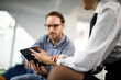 © Nikola Spasenoski - Business professionals discussing strategy and analysis using a tablet in a modern office setting during a work session in the afternoon