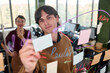 © TrueFrame Collective - Caucasian young adult man writing on transparent board with colorful markers while Caucasian young adult woman standing in background observing brainstorming session in modern office