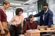 © TrueFrame Collective - Diverse group of young adult men and women collaborating around laptop in modern office, smiling and discussing project, multiethnic team engaging in teamwork and communication