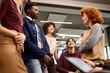 © TrueFrame Collective - Diverse group of young adults standing and sitting in modern office, engaging in conversation, smiling and interacting with each other