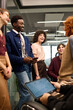 © TrueFrame Collective - Group of young adult multiethnic men and women standing and sitting in modern office, smiling and talking during informal meeting, one holding digital tablet