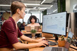 © TrueFrame Collective - Caucasian young adult woman working at computer with business analytics dashboard on screen, multiethnic young adult colleagues visible in modern office workspace
