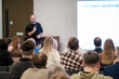 © Anton Gvozdikov - Vibrant conference room scene shows presenter addressing attentive audience during seminar with bright screen. Professional atmosphere highlights learning, collaboration, and business communication.
