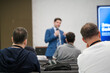 © Anton Gvozdikov - Presenter blue suit delivers talk to audience in conference room. Attendees listen, take notes, focus. Modern professional setting emphasizes learning and collaboration.