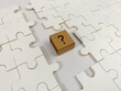 © HannaJ - A small cardboard cube with a printed question mark sits on a white jigsaw puzzle, representing missing information, business uncertainty, and finding strategic solutions.