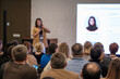 © Anton Gvozdikov - Presenter speaks to crowd during conference session. Audience seated listening while large screen shows profile slide. Collaborative learning and professional exchange emphasized.