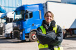 © Koldo_Studio - Female semi truck driver standing confident with crossed arms in front of fleet trucks at a cold storage warehouse