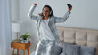 © Yuliia - Carefree Caucasian woman jumping dancing on bed listening music in earphones smiling moving hands party jump in bedroom home female girl listen headphones audio song sound holding mobile phone delight