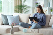 © PheelingsMedia - Serious woman in blue using digital tablet on a sofa