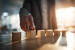 © Mykola - Professional man selecting a single wooden block from a row on a desk, a visual metaphor for choosing the right candidate in business with lens flare