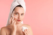 © New Africa - Beautiful woman with hair wrapped in towel applying cream on face against pink background. Space for text