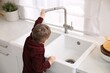 © New Africa - Child safety at home. Little boy opening faucet at sink in kitchen