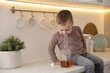 © New Africa - Child safety at home. Little boy with bottle of alcohol drink sitting on counter in kitchen, space for text